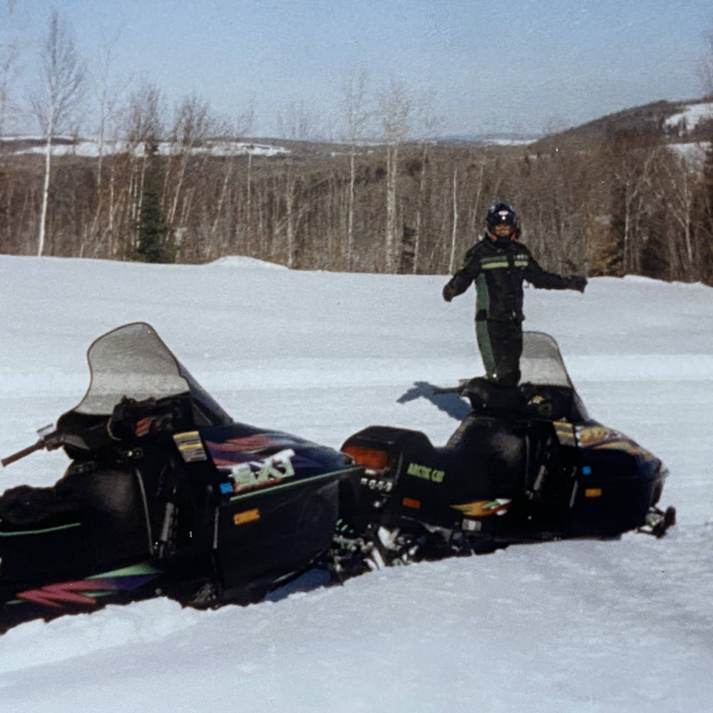 Man standing in snow behind two snow mobiles